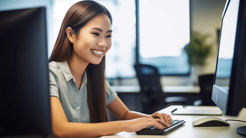 A woman smiles while reading something on her computer monitor